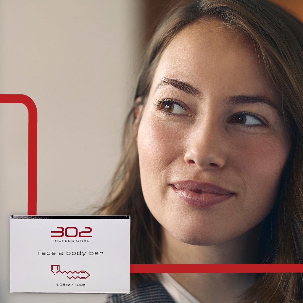 BAR-425OZ_WOMAN_3_1024x1024_72 | 302 Professional Skincare Portrait of a woman smiling beside a white skincare box labeled '302 Professional' for a face & body bar with red design accents on the background side panel.