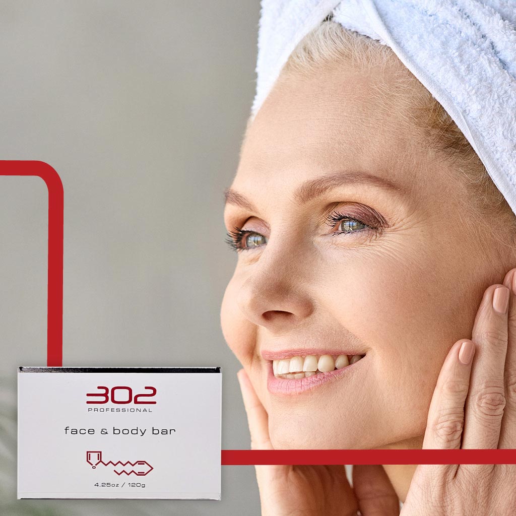 BAR-425OZ_WOMAN_4_1024x1024_72 | 302 Professional Skincare Smiling woman with a towel wrapped around her head beside a box labeled 302 Professional face & body bar.