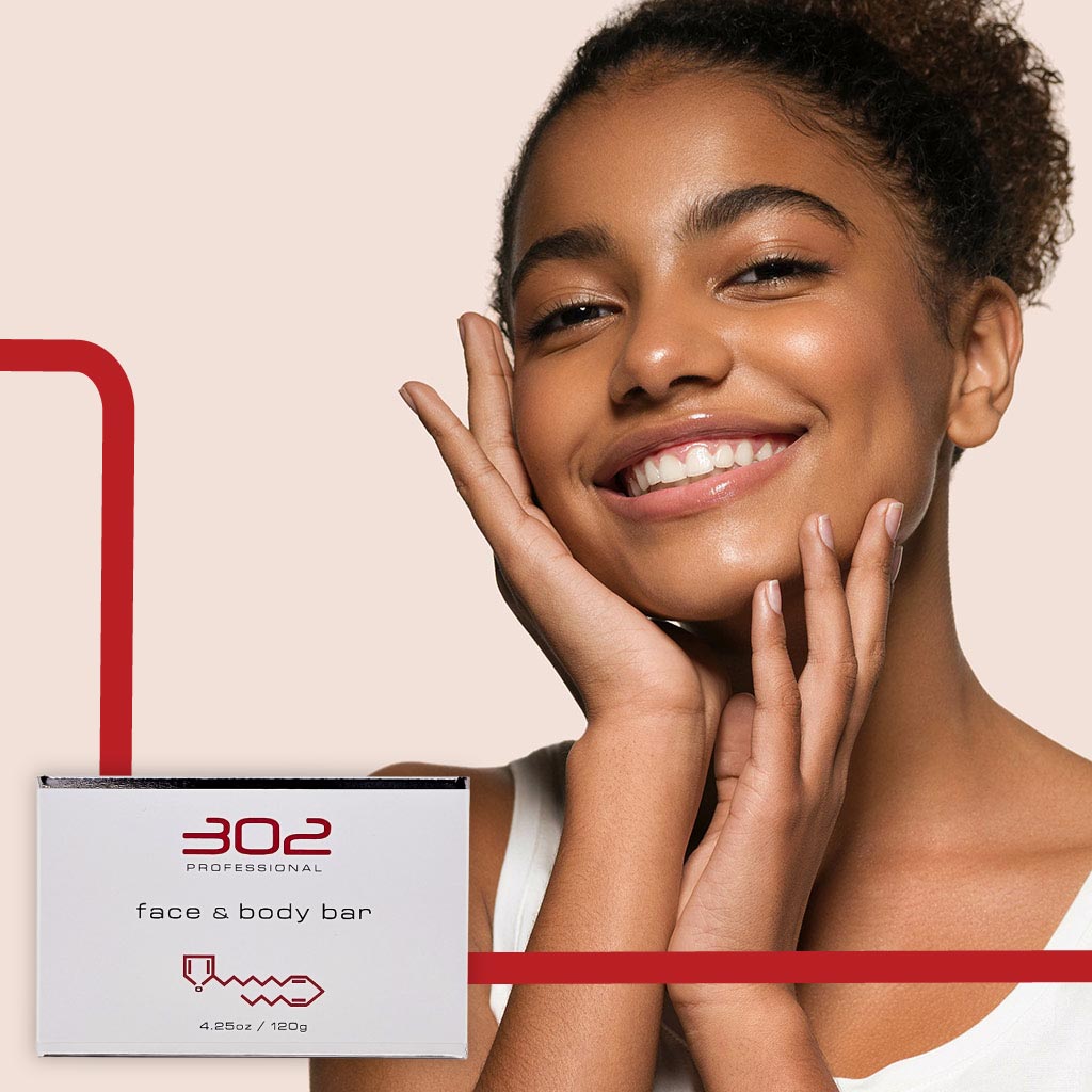 BAR-425OZ_WOMAN_5_1024x1024_72 | 302 Professional Skincare Smiling woman holds a box labeled '302 Professional face & body bar' against a pale pink background.