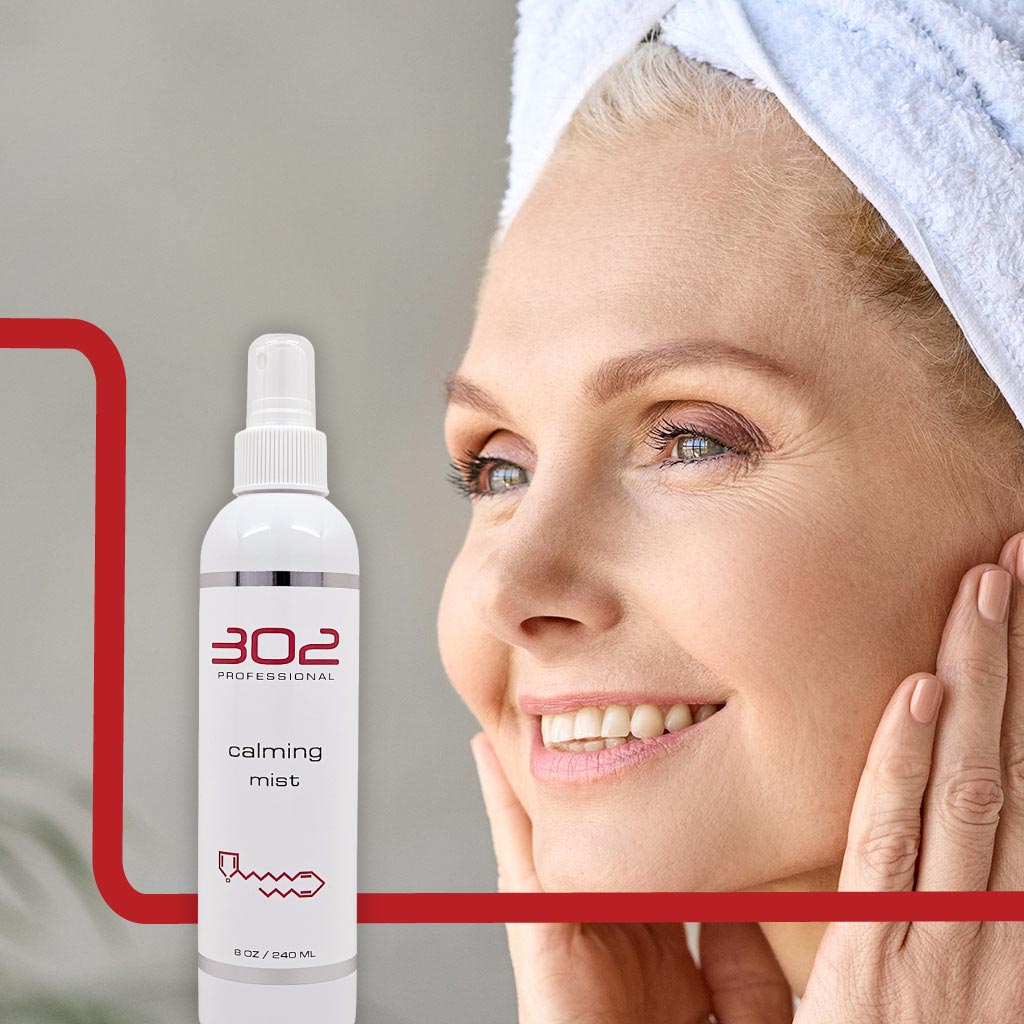 CALMING-MIST-8OZ_WOMAN_4_1024x1024_72 | 302 Professional Skincare Smiling woman with a towel on her head, next to a bottle labeled '302 Professional Calming Mist' on a light background.