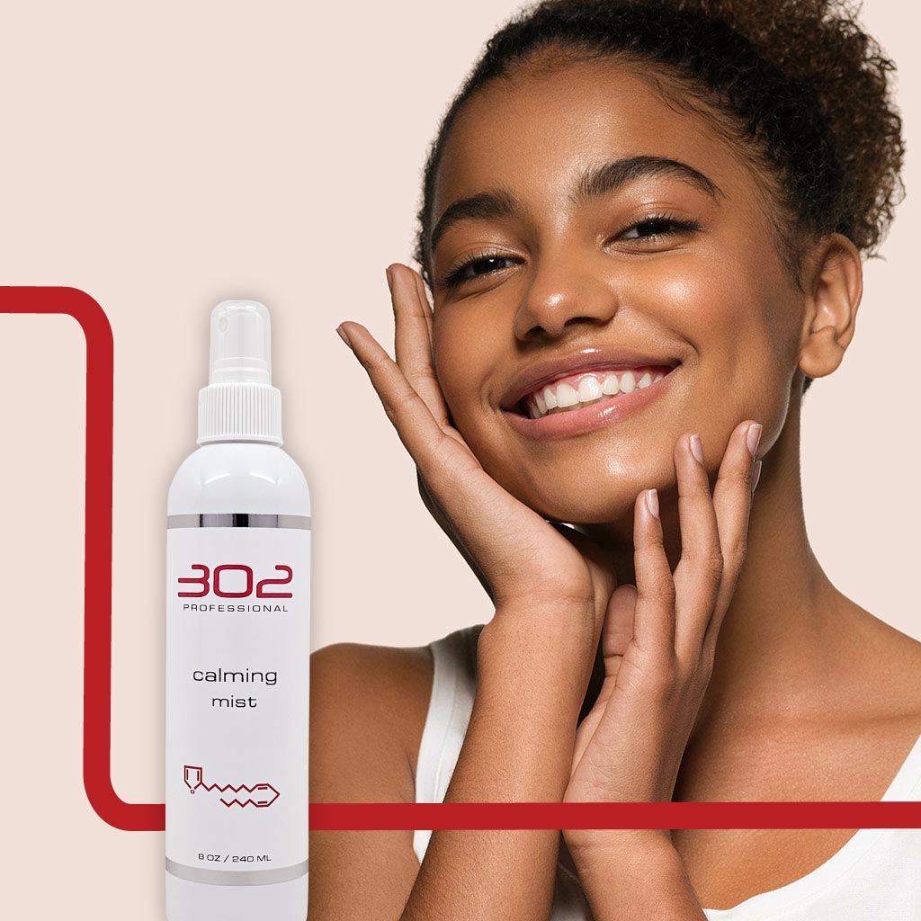 CALMING-MIST-8OZ_WOMAN_5_1024x1024_72 | 302 Professional Skincare Smiling woman holding her face beside a white spray bottle labeled '302 Professional calming mist' on a beige background.