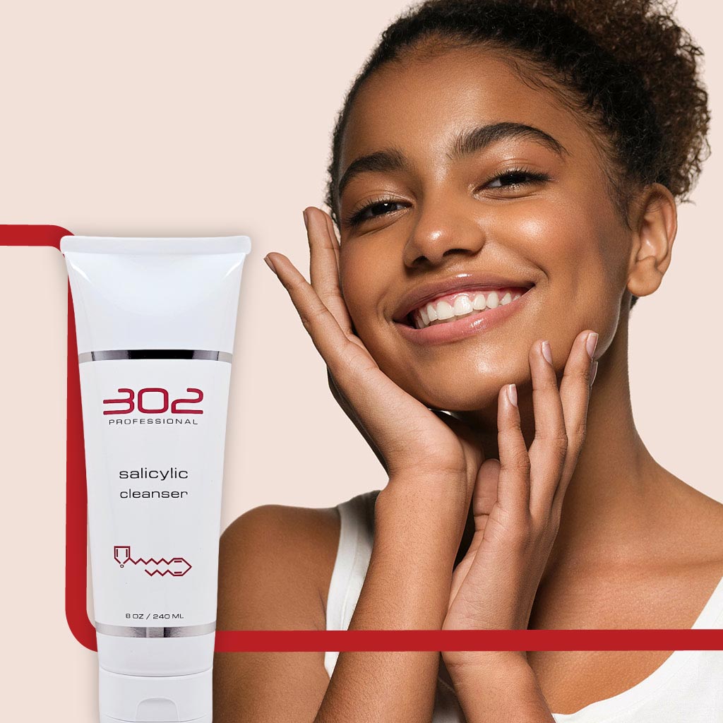 SALICYLIC-CLEANSER-8OZ_WOMAN_5_1024x1024_72 | 302 Professional Skincare Smiling woman beside a tube of 302 Professional Salicylic Cleanser on a pale background