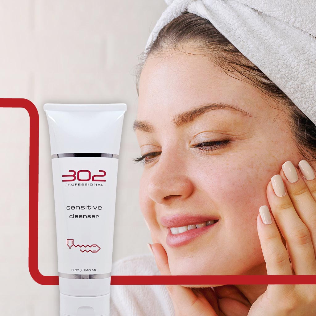 SENSITIVE-CLEANSER-8OZ_WOMAN_2_1024x1024_72 | 302 Professional Skincare Close-up of a woman with a towel on her head beside a white tube labeled '302 Professional sensitive cleanser' in a skincare setting.