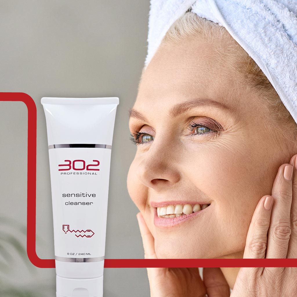 SENSITIVE-CLEANSER-8OZ_WOMAN_4_1024x1024_72 | 302 Professional Skincare Smiling woman with a towel on her head next to a tube labeled '302 Professional' and 'sensitive cleanser'.