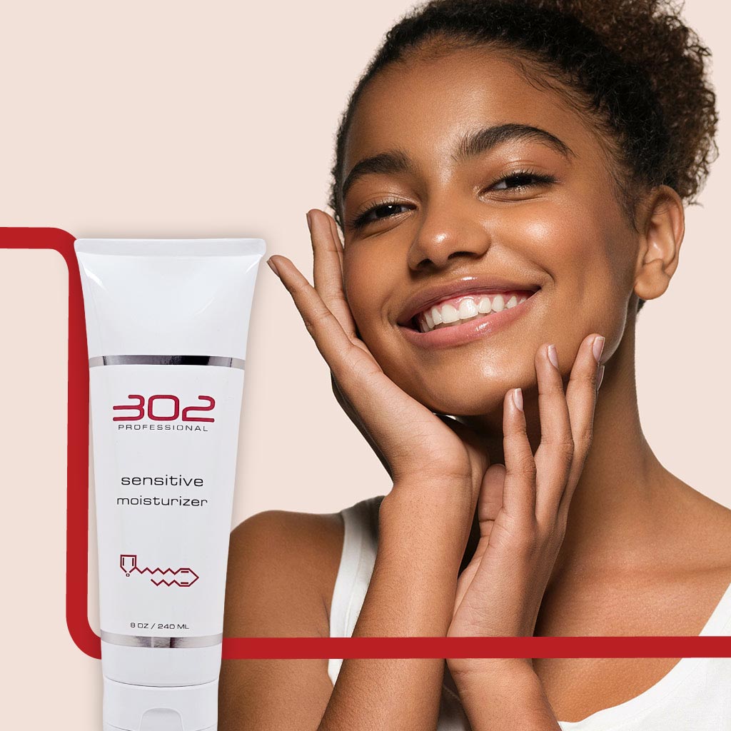 SENSITIVE-MOISTURIZER-8OZ_WOMAN_5_1024x1024_72 | 302 Professional Skincare Smiling woman with hands near her face next to a white tube labeled '302 Professional sensitive moisturizer' against a light beige background, product in focus.